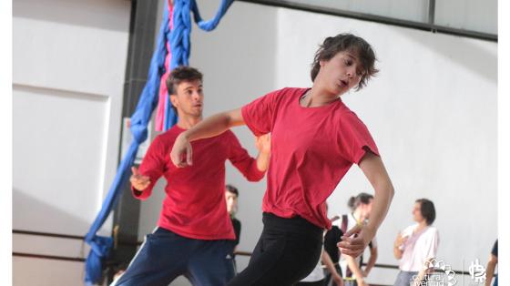 Estudiantes en clases de la Escuela de Danza, Teatro y Circo Dos jóvenes con camisa roja realizando movimientos con los brazos en clases de teatro