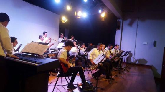 Concierto Navideño - Banda de Conciertos de Limón Músicos de la Banda de Conciertos de Limón tocando sobre un escenario de madera, una tenue luz color violeta baña a los músicos.
