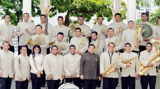 Ensamble de la Banda de Conciertos de Guanacaste. Los músicos sonríen con sus instrumentos en mano, detrás de ellos el kiosco del parque central de Liberia.