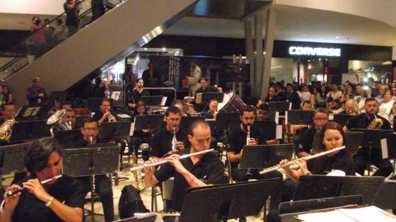 Músicos de la Banda de Conciertos de Cartago tocando en una sala de un mall rodeados de mucho público.