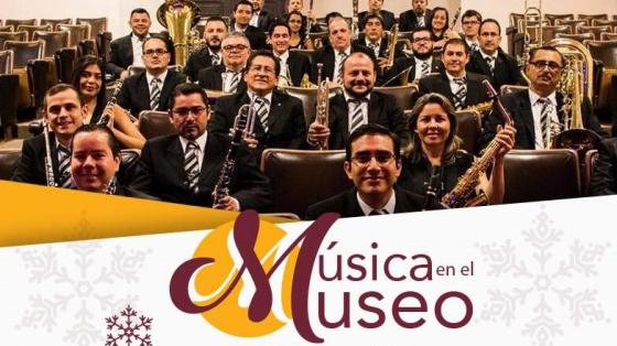 Músicos y músicas sentados en las butacas del Museo Juan Santamaría viendo a la cámara sonriendo. La foto contiene adornos navideños para resaltar la festividad.