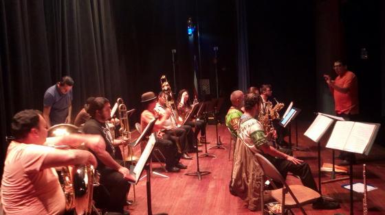Concierto Navideño - Banda de Conciertos de Limón Músicos vistos de perfil tocando en un escenario con tenue luz rojiza sobre ellos mientras tocan su programa musical.