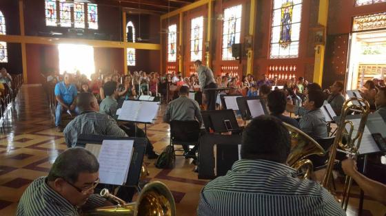 Músicos de la Banda tocando dentro de un templo. La luz del sol atraviesa los vitrales y el lugar se alumbra de una manera especial.