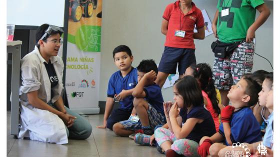 Niños sentados en el piso poniéndole atención a un joven vestido de científico