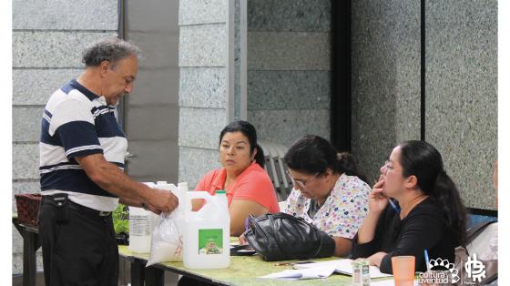 Señor sacando material de una bolsa, al lado con botellas y tres personas observando lo que realiza 