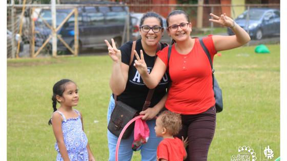 Dos mujeres sonriendo mientras miran a la cámara, al lado tienen dos niños