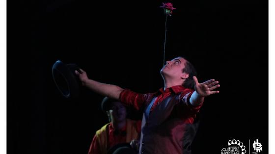 Actor haciendo malabares, con mentón sostiene una flor desde su tallo y en su mano derecha un sombrero