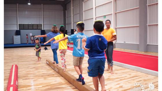 Niños en fila caminando sobre una barra de gimnasia