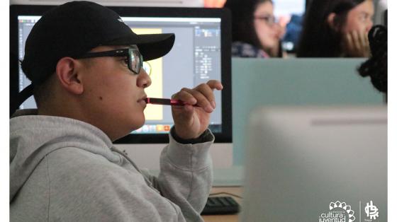 Joven prestando atención a una clase, detrás de él una computadora