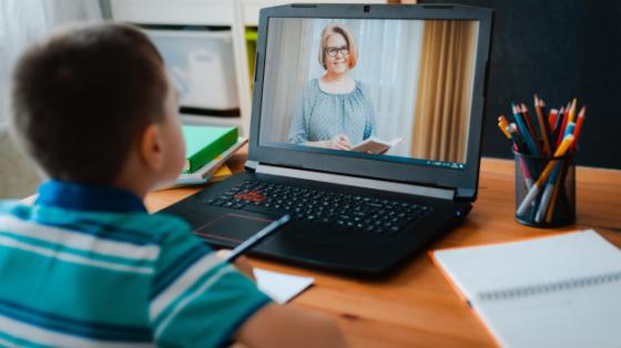 Niño frente a computadora mientras su profesora da clases