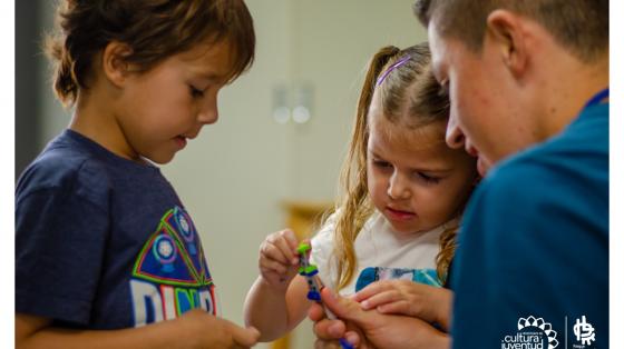 Taller de experimentos "El mundo de la ciencia desde el aula virtual" Una niña y un niño junto a un adulto armando un proyecto