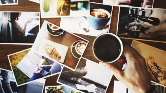 UNa mano sostiene una taza de café y sobre la mesa muchas fotografías en desorden