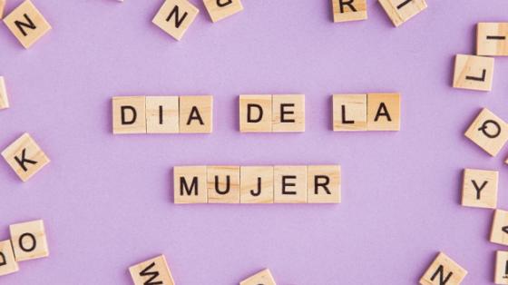 Charla "Día internacional de la mujer" Letras sueltas en madera que forman la frase "Día de la mujer", en fondo lila