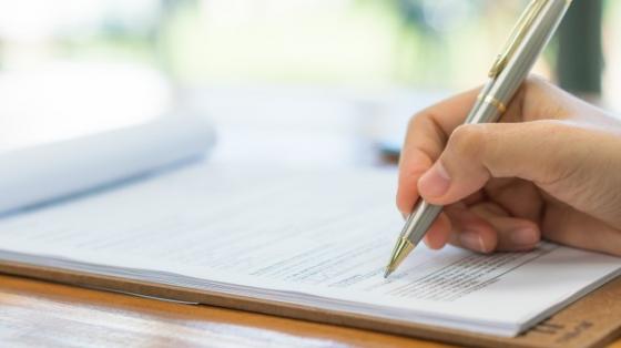 Mano con una pluma, escribiendo sobre unas hojas blancas