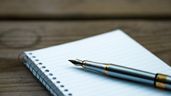Libreta abierta y lapicero pluma sobre superficie de madera. 