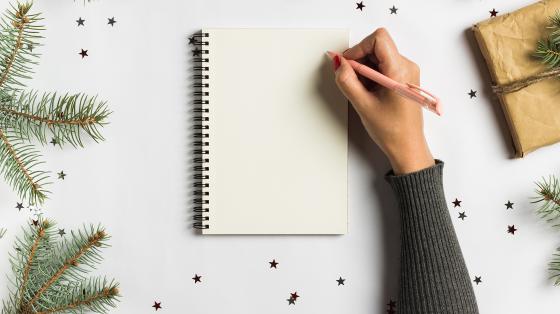 Mano escribiendo en una libreta en un fondo navideño