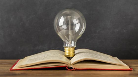 Libro con una bombilla en el medio Fotografía con un fondo gris de un libro abierto a la mitad y en el medio se encuentra una bombilla eléctrica.