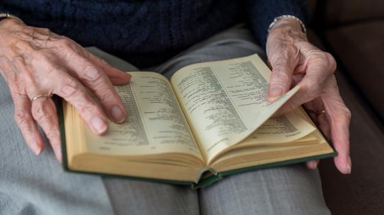 Persona adulta leyendo Fotografía de una persona adulta mayor leyendo un libro. En la fotografía solo se hace un plano del regazo de la persona donde se ve el libro y sus manos sosteniéndolo.