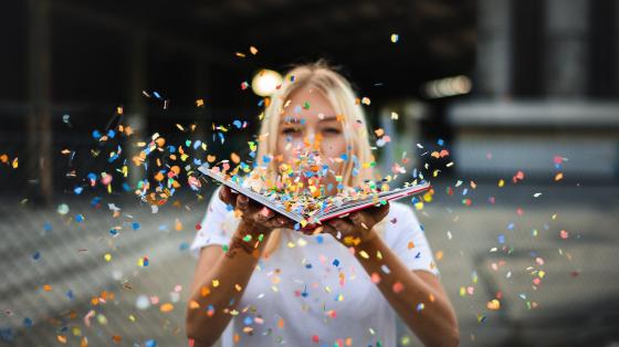 Soplando confeti. Fotografía de una mujer soplando confeti desde un libro abierto.