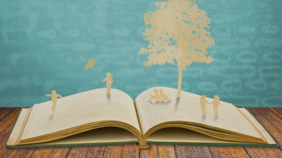 Presentación de los libros "Fábulas desde el bosque en Costa Rica" y "Regresan los pájaros" Fondo celeste. Sobre una mesa de manera un libro abierto con figuras de papel.