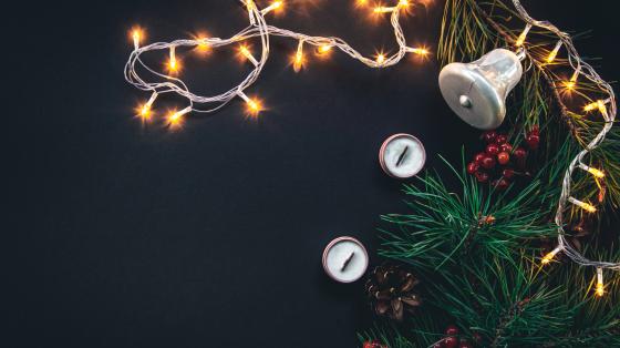 Fondo negro. Luces de navidad, cancelas y una guirnalda con una campana y bellotas.
