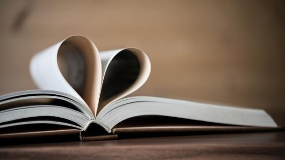 Fondo difuminado. Libro abierto con sus páginas en forma de corazón sobre una mesa de madera.
