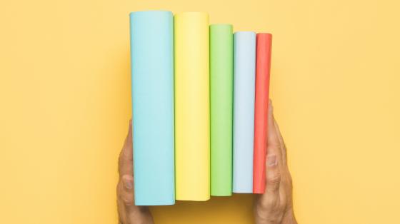 Fondo amarillo. Dos manos sostienen 5 libros de manera vertical. 