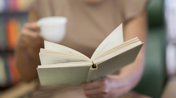 Tertulia: La política en la cotidianidad Persona de fondo difuminada con una taza y sosteniendo un libro en primer plano.