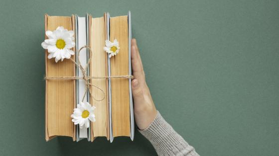 Recital Internacional de Poesía Hojas sin Tiempo Fondo gris. Desde vista superior unos libros decorados con flores y una mano los sostiene.
