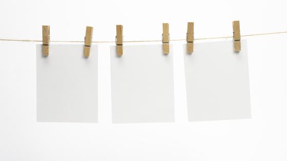 Exposición de fotografías "Materialidades" Fondo blanco. Una cable sosteniendo con prensas tres tarjetas blancas.