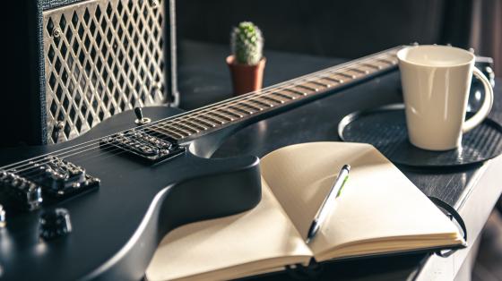 IV Conversatorio sobre Música Costarricense: Música rock, pop, experimental Sobre una mesa, se encuentra un parlante, una guitarra eléctrica y un libro de notas.