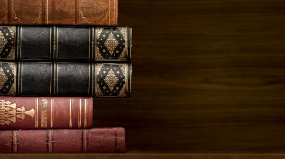 Exposición de ilustraciones "Del Infierno al Cielo: A más de 500 años de la Divina Comedia de Dante Alighieri" Torre de libros antiguos en fondo de madera.