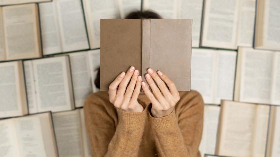 Fondo de libros abiertos. Persona sosteniendo el libro tapando su cara. 