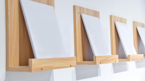 Exposición de arte e ilustración del Grupo 506 Fondo blanco. Repisa de madera sosteniendo un cuadro blanco.