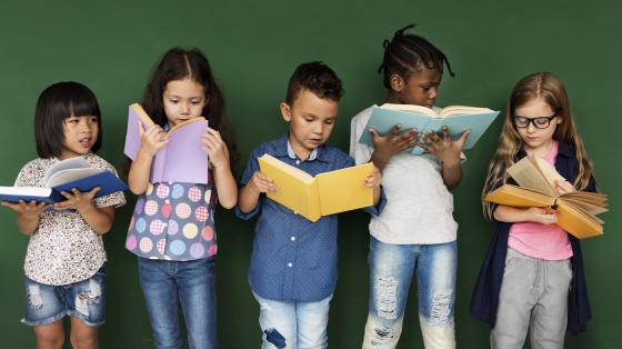 Vacaciones en mi biblioteca Grupo de niños leyendo un libro.