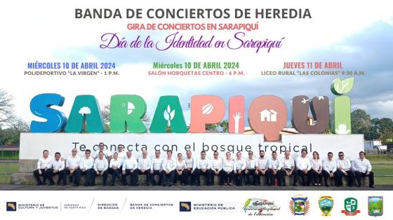 Músicos de la Banda de Heredia sentados en fila bajo las letras gigantes que dicen Sarapiquí