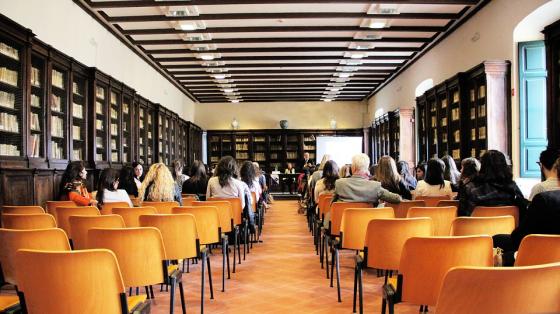 Un auditorio visto desde el fondo a los costados estantes con libros y varias personas sentadas