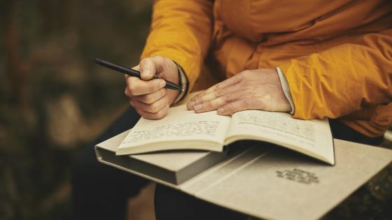 Parte de una persona conos libros sobre los regazos y sostiene una pluma