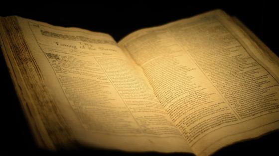 Exposición "Las Mujeres en el Quijote" Un libro abierto antiguo iluminado con una luz amarilla