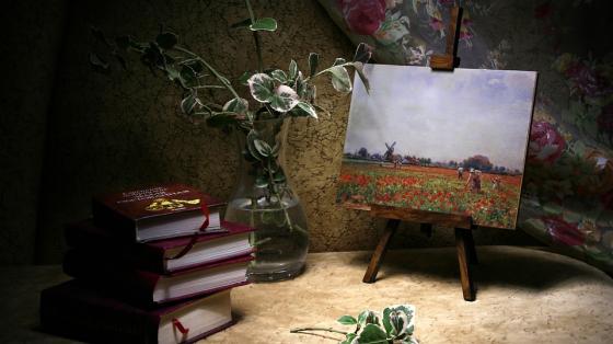 Un bastidor con una pintura de un paisaje, un florero y unos libros apilados