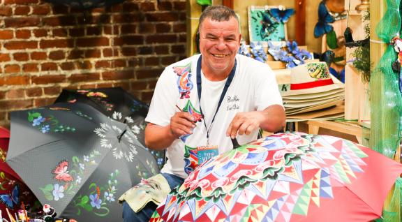 Se muestra a hombre artesano decorando con pintura una sombrilla 