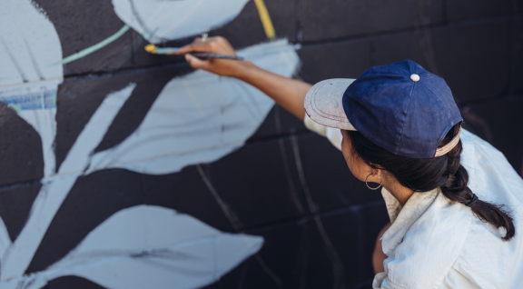 Mujer cabello trenzado gorra azul pintando mural