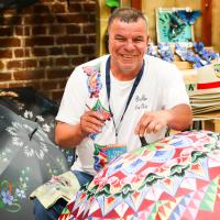 Se muestra a hombre artesano decorando con pintura una sombrilla 