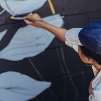 Mujer cabello trenzado gorra azul pintando mural