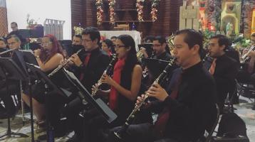 Músicos de la Banda de Conciertos de Alajuela en plena ejecución musical, sentados y vestidos de negro con adornos y luces navideña a su alrededor.