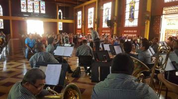 Músicos de la Banda tocando dentro de un templo. La luz del sol atraviesa los vitrales y el lugar se alumbra de una manera especial.
