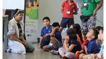 Niños sentados en el piso poniéndole atención a un joven vestido de científico