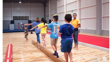 Niños en fila caminando sobre una barra de gimnasia