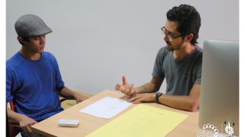 Dos personas conversando, una de ellas explicándole a otra mientras revisan un documento
