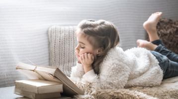 Niña leyendo un libro sobre el sofá